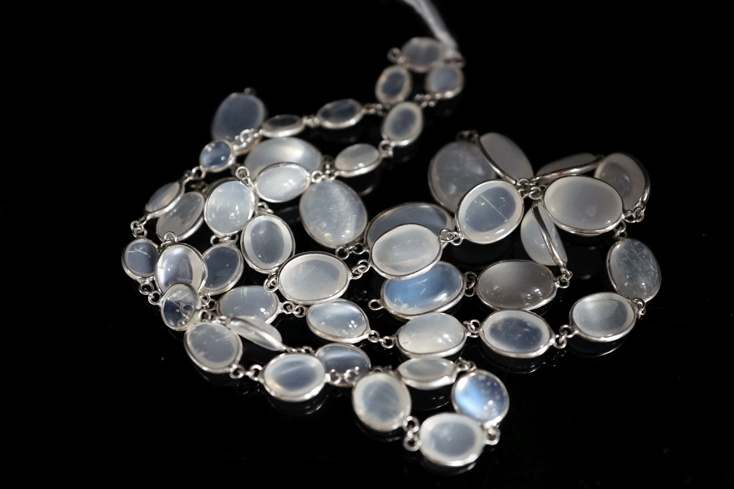 A modern (1980's) white metal and graduated moonstone set spectacle necklace, 69cm.